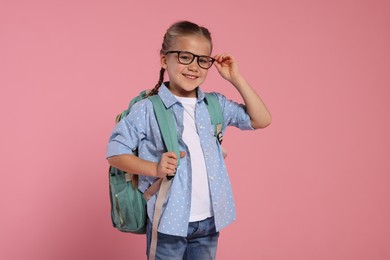 Happy schoolgirl in glasses with backpack on pink background