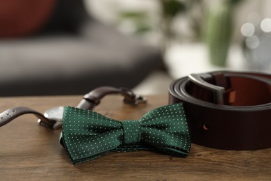 Photo of Stylish green bow tie, wristwatch and belt on wooden table, closeup