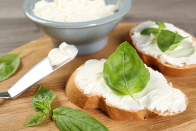 Photo of Delicious sandwiches with cream cheese and basil leaves on wooden table, closeup