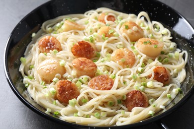 Delicious scallop pasta with green onion on grey table, closeup