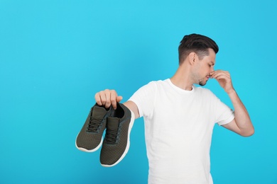 Man feeling bad smell from shoes on color background. Air freshener