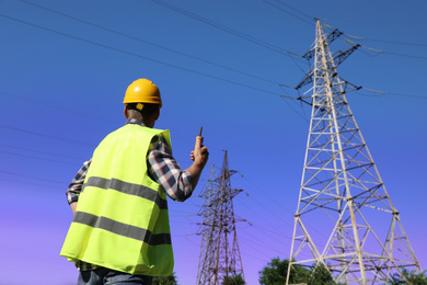 Professional electrician with portable radio station near high voltage tower