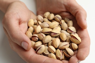 Woman holding tasty roasted pistachio nuts on white background, closeup