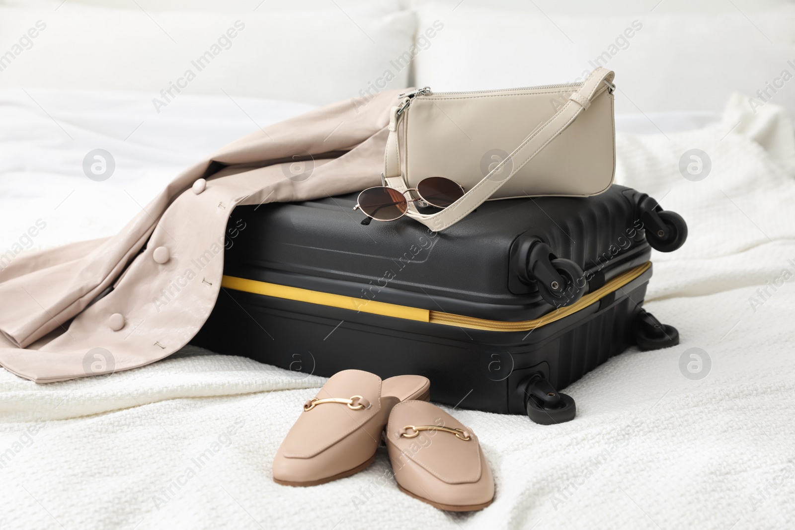 Photo of Suitcase packed for trip, shoes, jacket and fashionable accessories on bed in room