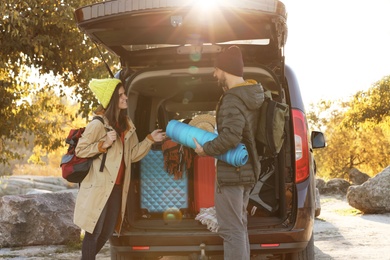 Young couple with camping equipment near car trunk outdoors