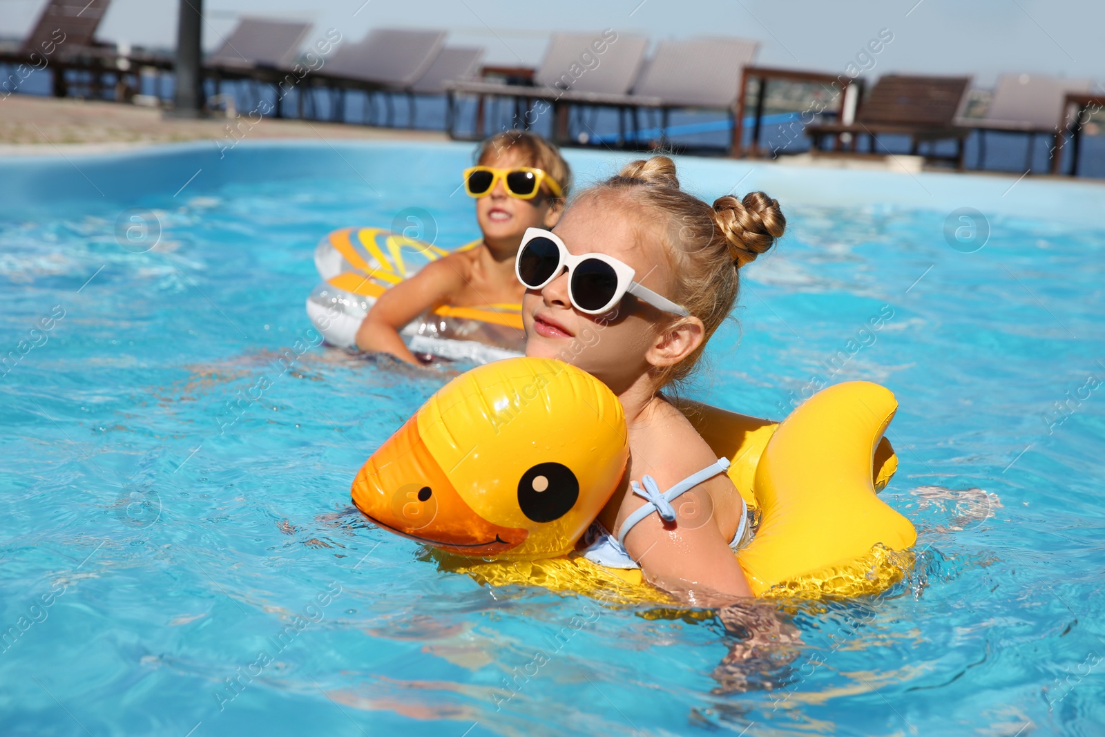 Photo of Happy children with inflatable rings in outdoor swimming pool on sunny summer day