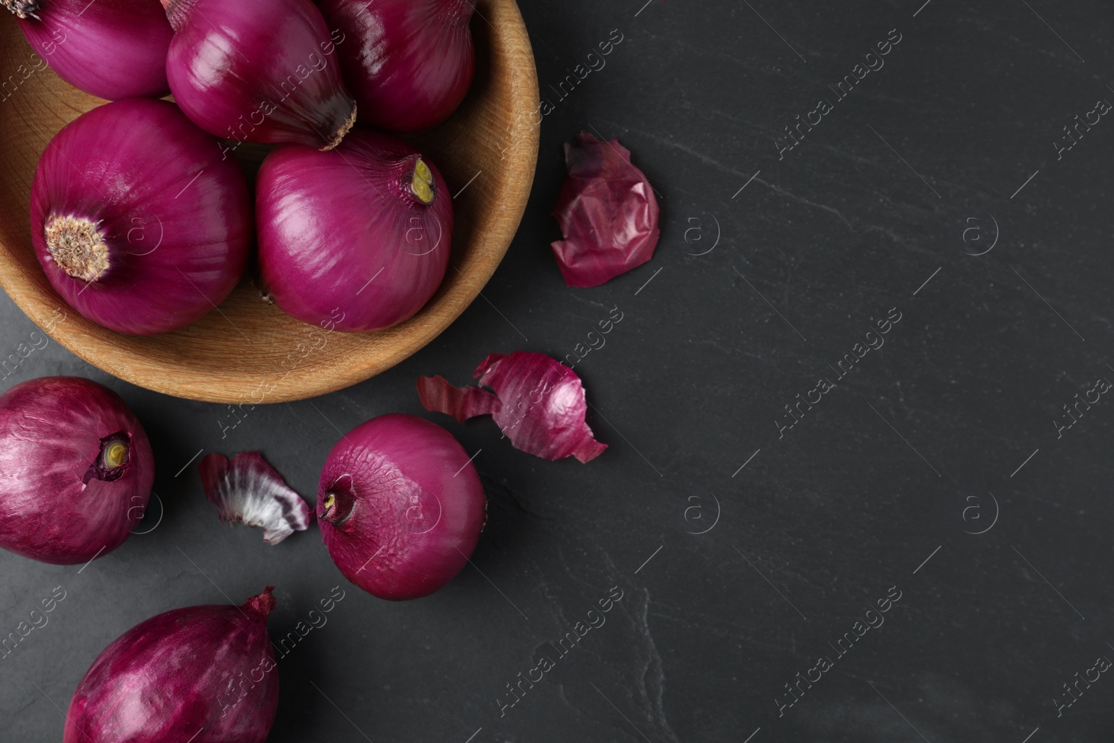 Photo of Ripe red onion bulbs and bowl on black table, flat lay. Space for text