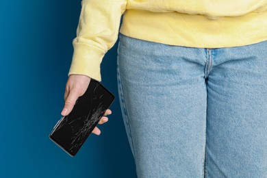 Woman holding damaged smartphone on light blue background, closeup. Device repairing