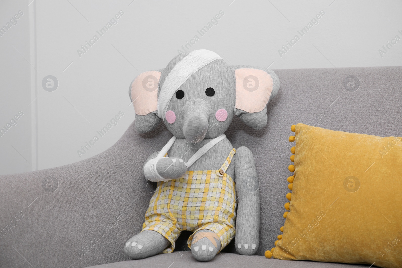 Photo of Toy elephant with bandages sitting on sofa near light wall
