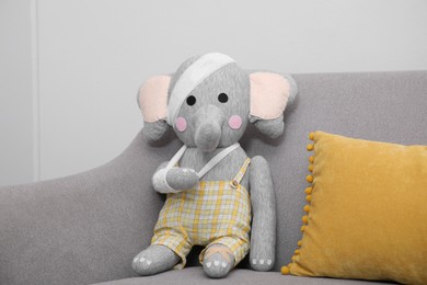 Toy elephant with bandages sitting on sofa near light wall