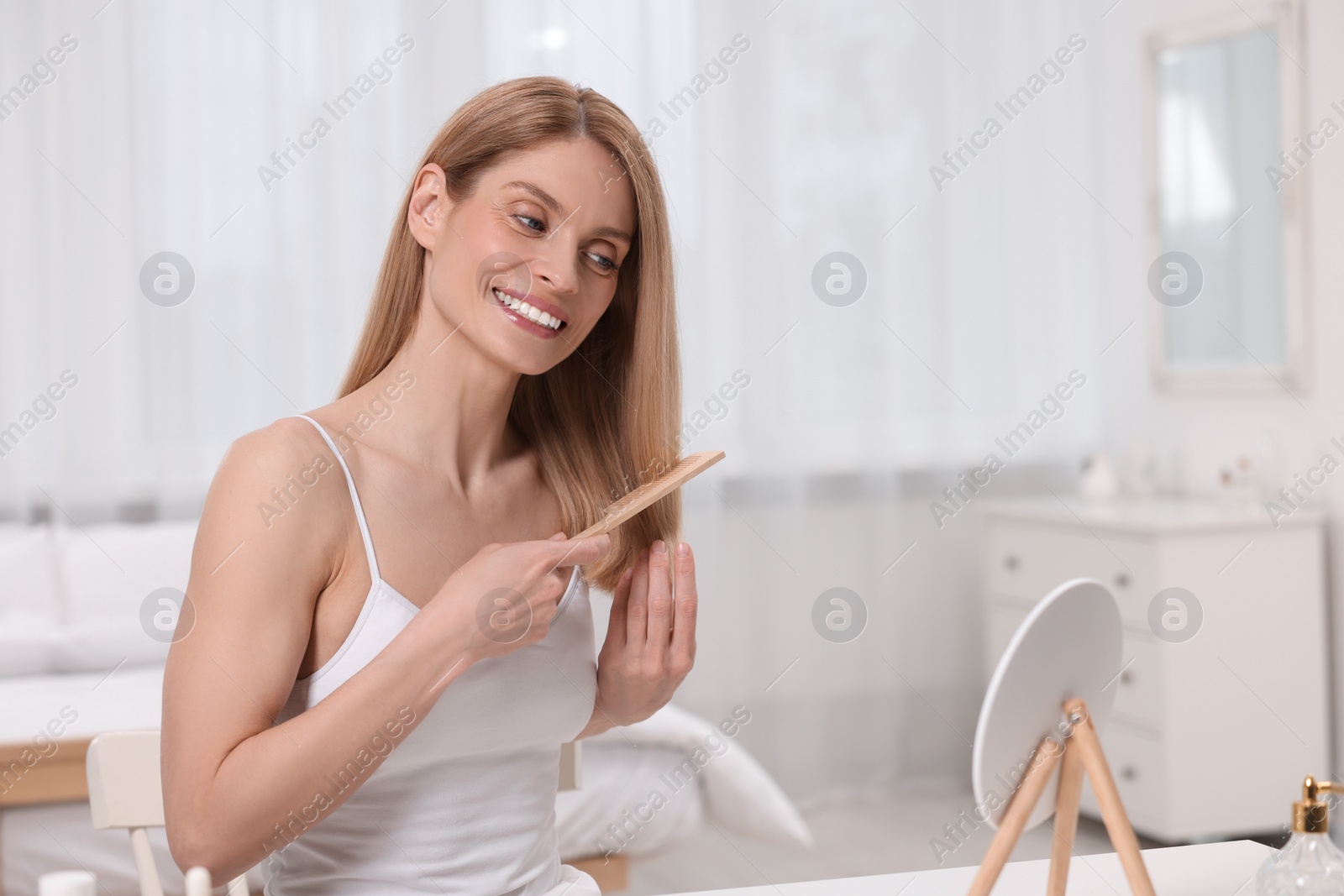 Photo of Beautiful woman brushing her hair near mirror in bedroom. Space for text