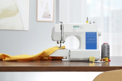 Photo of Sewing machine with fabric and craft accessories on wooden table indoors