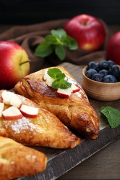 Photo of Fresh tasty puff pastry with blueberries, apples and mint served on wooden table, closeup