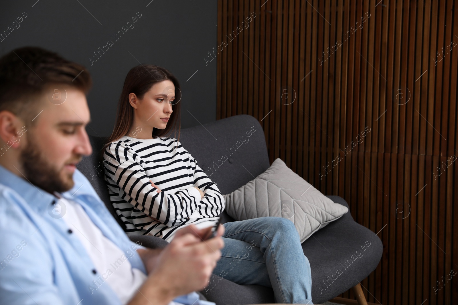 Photo of Young man preferring smartphone over his girlfriend at home. Relationship problems