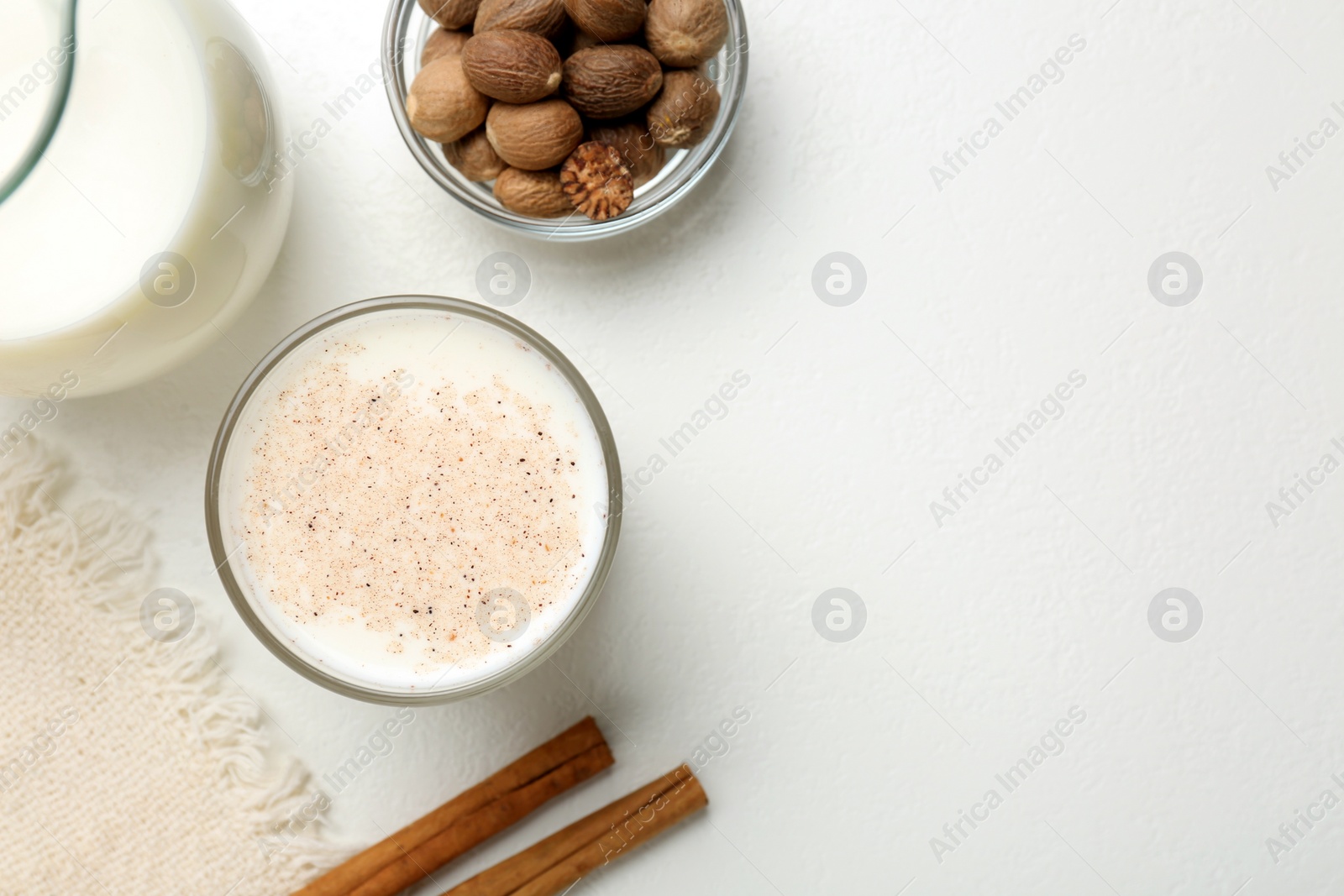 Photo of Milk with nutmegs and cinnamon on white table, flat lay. Space for text