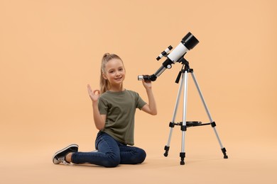Photo of Happy little girl with telescope showing ok gesture on beige background