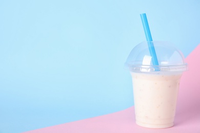 Photo of Tasty milk shake in plastic cup on color background. Space for text