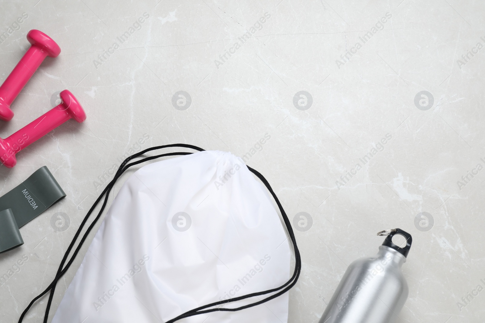 Photo of White drawstring bag, thermo bottle and dumbbells on light marble background, flat lay. Space for text