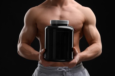 Photo of Young man with muscular body holding jar of protein powder on black background, closeup