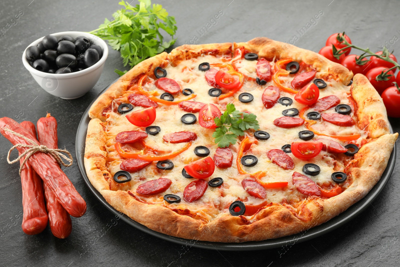 Photo of Tasty pizza with dry smoked sausages, olives, tomatoes, pepper and parsley on grey table