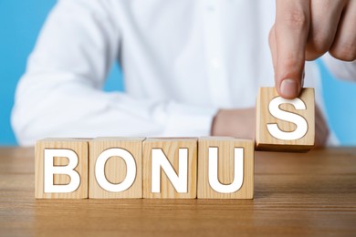 Image of Man making word Bonus of cubes with letters on wooden table, closeup