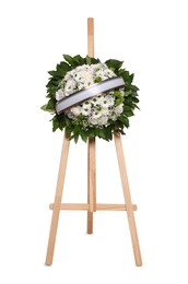 Photo of Funeral wreath of flowers with ribbon on wooden stand against white background