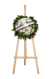 Funeral wreath of flowers with ribbon on wooden stand against white background