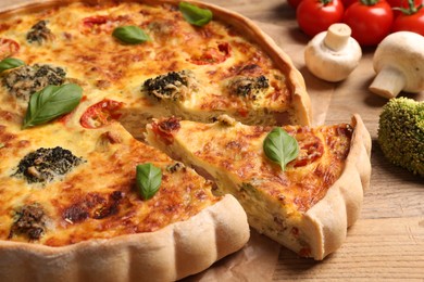 Photo of Delicious homemade vegetable quiche and ingredients on wooden table, closeup