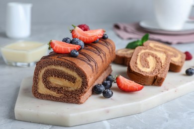 Photo of Tasty chocolate cake roll with cream and berries on light grey marble table