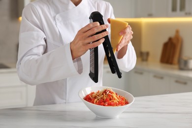 Professional chef grating cheese into delicious dish at white marble table indoors, closeup