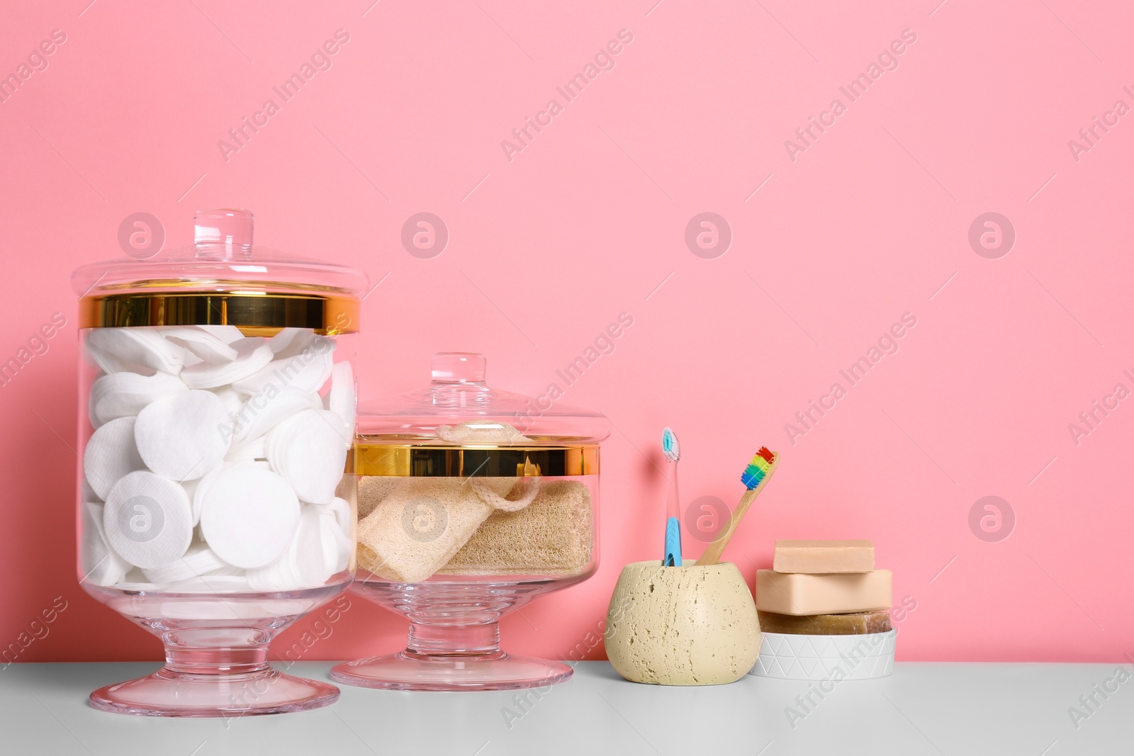 Photo of Composition of glass jar with cotton pads on table near pink wall. Space for text