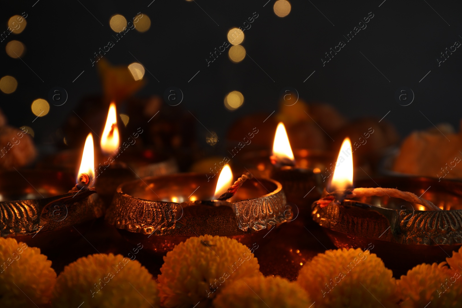 Photo of Diwali celebration. Diya lamps and chrysanthemum flowers on table against blurred lights, closeup