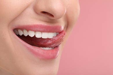 Photo of Young woman licking her teeth on pink background, closeup