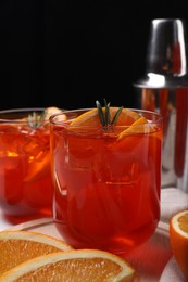 Aperol spritz cocktail, ice cubes, rosemary and orange slices in glasses on table, closeup