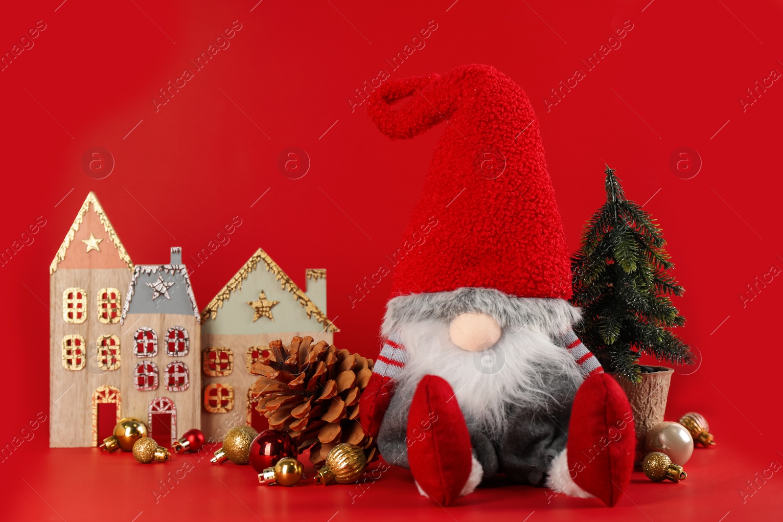 Photo of Cute Christmas gnome, small decorative fir tree and festive decor on red background