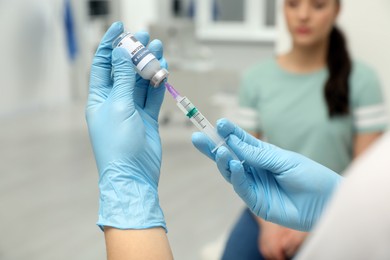 Woman waiting to get hepatitis vaccine at clinic. Doctor filling syringe from glass vial, closeup