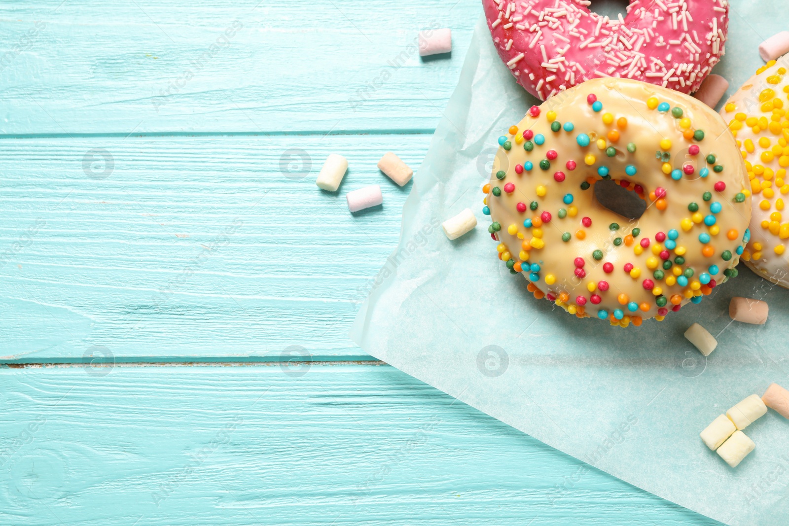 Photo of Delicious glazed donuts on blue wooden table, flat lay. Space for text