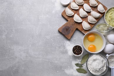 Photo of Raw dumplings (varenyky) and ingredients on grey table, flat lay. Space for text