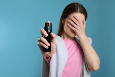 Young woman covering eyes with hand and using pepper spray on light blue background