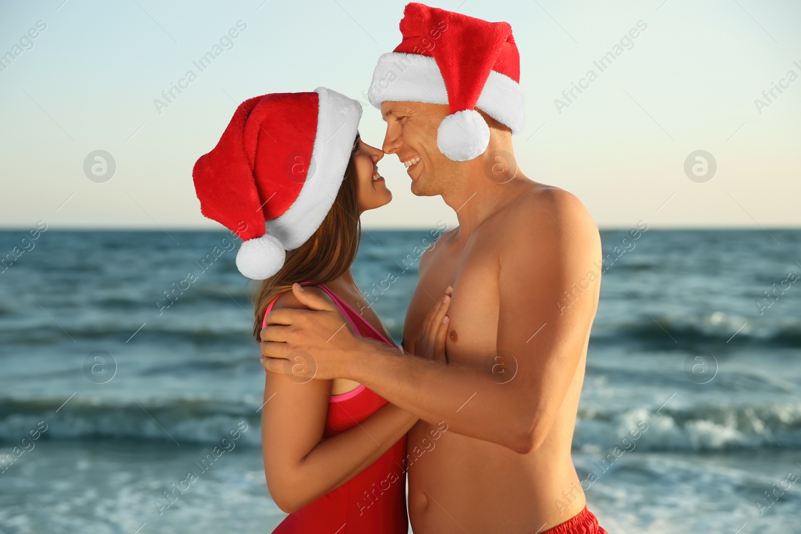 Photo of Happy couple with Santa hats together on beach. Christmas vacation