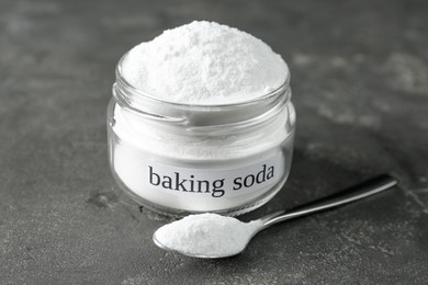 Photo of Jar and spoon with baking soda on grey table, closeup