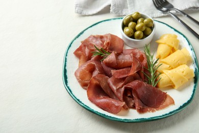 Photo of Delicious bresaola, cheese, olives and rosemary on light textured table. Space for text
