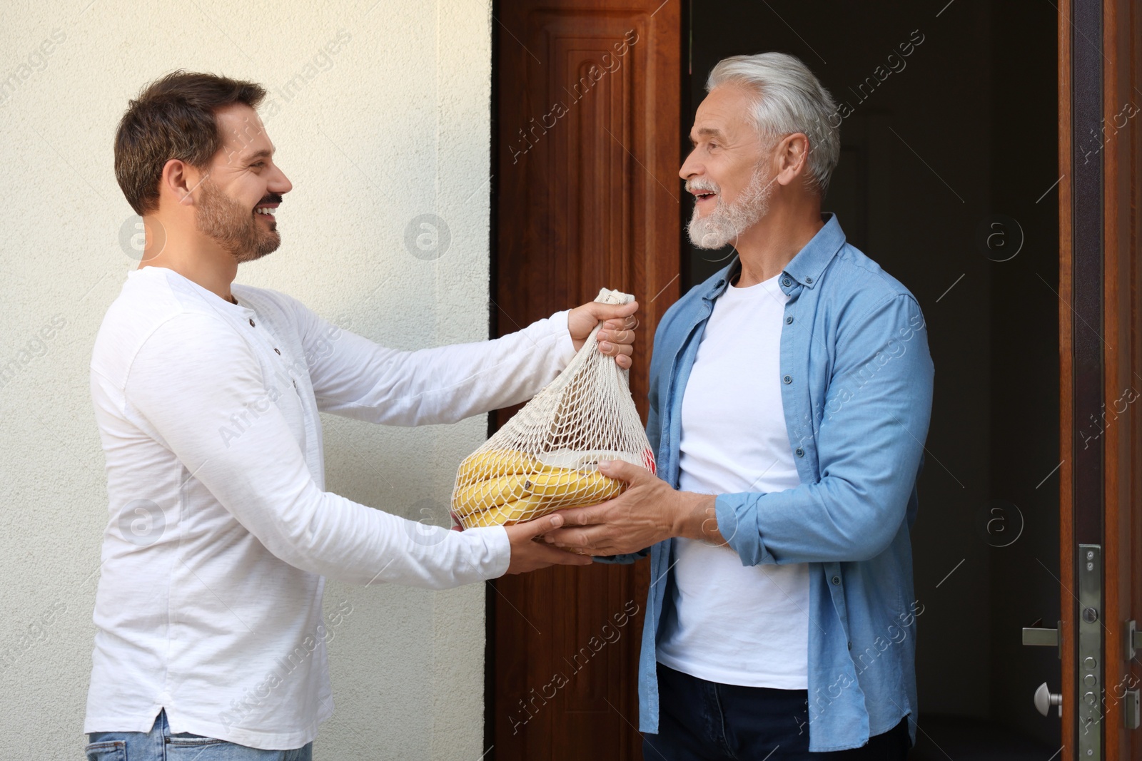 Photo of Man with net bag of products helping his senior neighbour outdoors