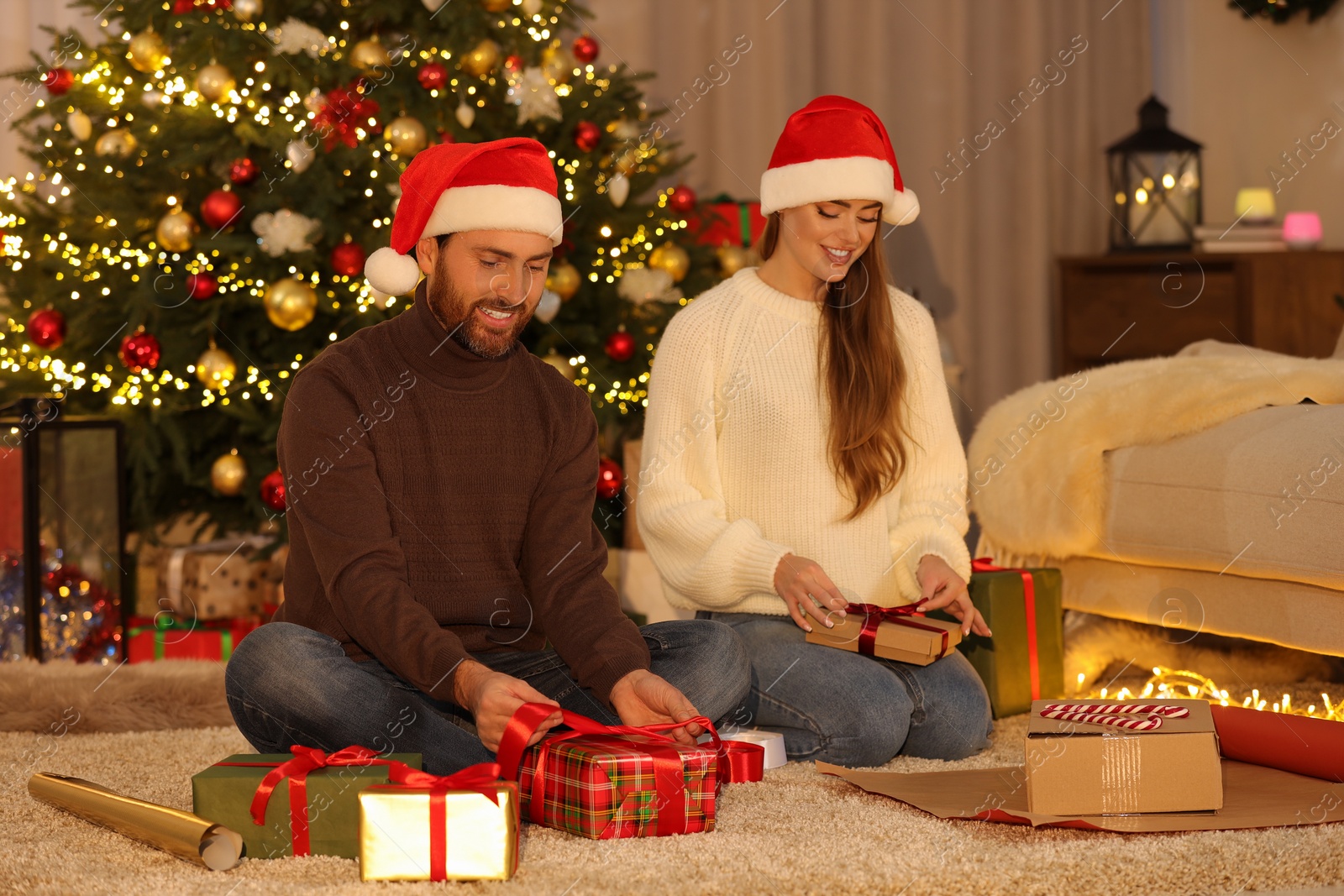 Photo of Happy couple in Santa hats decorating Christmas gift at home