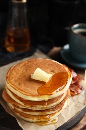 Photo of Delicious pancakes with maple syrup, butter and fried bacon on wooden board, closeup