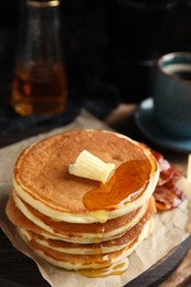 Delicious pancakes with maple syrup, butter and fried bacon on wooden board, closeup