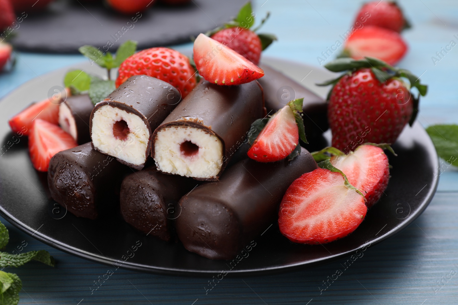 Photo of Delicious glazed curd snacks with fresh strawberries and mint on light blue wooden table, closeup