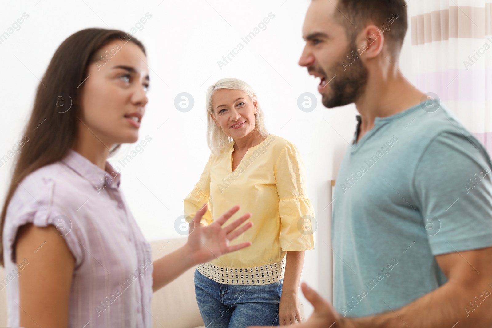 Photo of Young couple having argument in presence of mother-in-law at home. Family quarrel