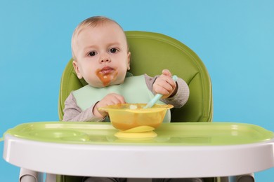 Cute little baby eating healthy food in high chair on light blue background
