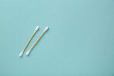 Photo of Two wooden cotton buds on turquoise background, flat lay. Space for text